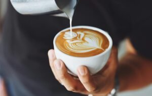 Close-up of a barista pouring milk to create latte art in a coffee cup.